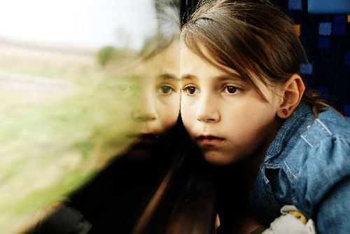 Girl in a classroom sadly looking outside the window.