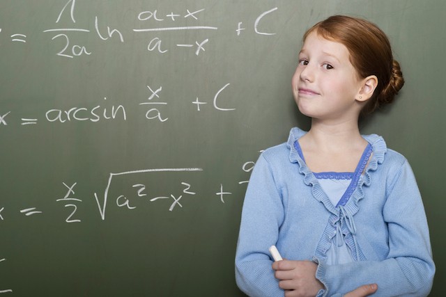 Young girl at a chalkboard solving a difficult problem confidentally.